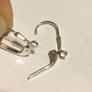 May include: Two silver earring hooks, one with a closed loop and the other with an open loop. The hooks are made of metal and are designed for attaching earrings.