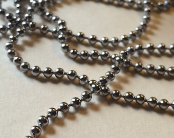 May include: A silver chain made of small, round beads. The chain is lying on a white surface.