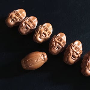 May include: A set of eight wooden beads, each carved with a different smiling face. The beads are brown and have a natural wood finish.