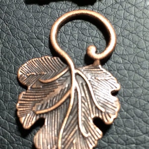May include: A copper-toned metal clasp with a grapevine design. The clasp features a leaf and a stem with grapes. The clasp is perfect for jewelry making or other craft projects.