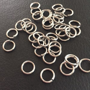 May include: A pile of silver jump rings, a type of metal ring used in jewelry making.