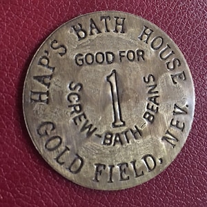 May include: A brass token with the text "Hap's Bath House" and "Good for 1 Screw-Bath Beans" around the edge. The token also says "Gold Field, Nev."
