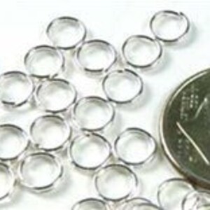 May include: A close-up of a pile of silver jump rings, with a US quarter for scale. The jump rings are small and round, and they are perfect for connecting jewelry pieces.