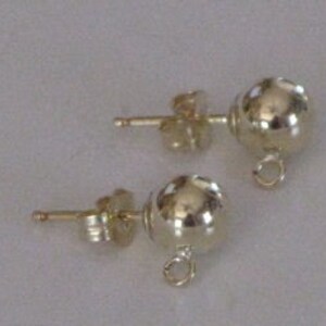 May include: A pair of gold-toned ball stud earrings with a small loop on the bottom of each ball. The earrings are designed for hanging charms or pendants.