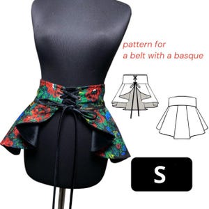 Op de afbeelding: Een bloemenriem met een basque, weergegeven op een zwarte mannequin. De riem heeft rode, groene en blauwe bloemen op een zwarte achtergrond, met een veter aan de voorkant en een klein maatlabel.