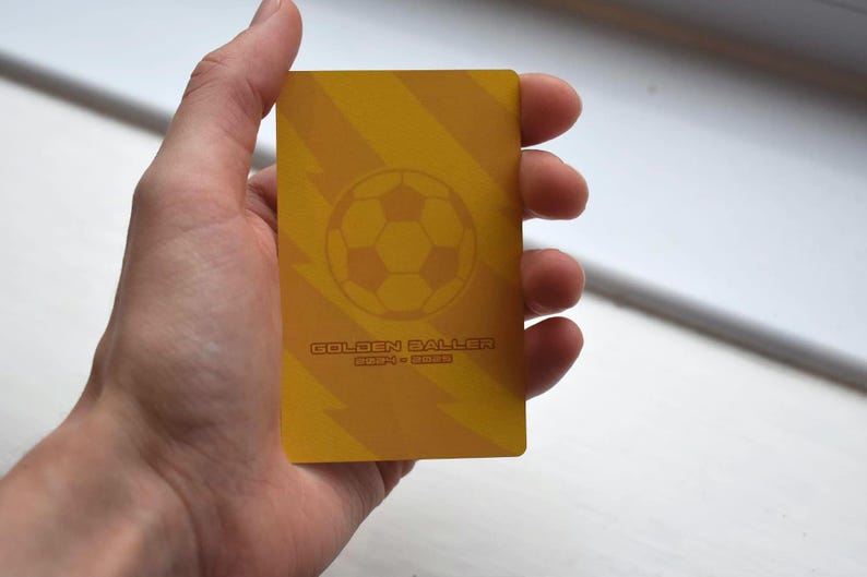 May include: A yellow card with a soccer ball graphic and the text "Golden Baller" in red. The card has a striped pattern.