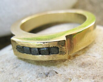 Può includere: Un anello a fascia d'oro con una fila di diamanti neri incastonati nella fascia.