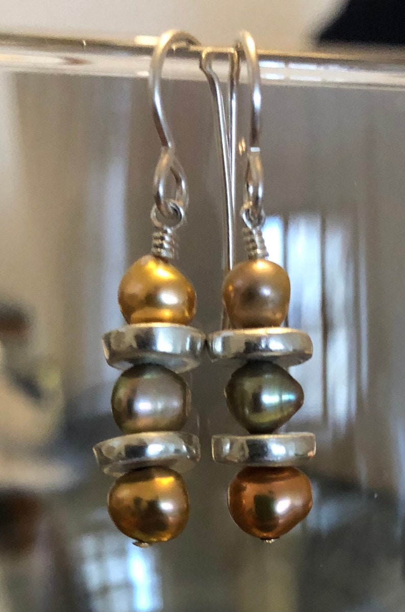 May include: Silver dangle earrings with three stacked beads. The top and bottom beads are gold, and the middle bead is a light green color.