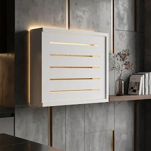 Puede incluir: Un aplique de pared rectangular blanco con cinco lamas horizontales que emiten una luz cálida. La lámpara está montada sobre una pared con textura de hormigón gris, con detalles metálicos verticales en tono dorado e iluminación integrada.