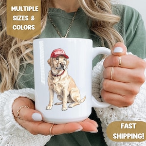 May include: White ceramic mug with a yellow Labrador Retriever wearing a red "MAGA" hat. The dog is sitting and looking to the right.
