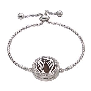 Puede incluir: Un brazalete ajustable de plata con un dije redondo que presenta un par de alas de ángel. El dije está decorado con diamantes de imitación transparentes.