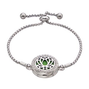 May include: Silver-toned adjustable bracelet featuring a round pendant with a lotus flower design. The pendant is encrusted with small, clear crystals and has a green interior. The bracelet has a chain-link design and adjustable ball ends.