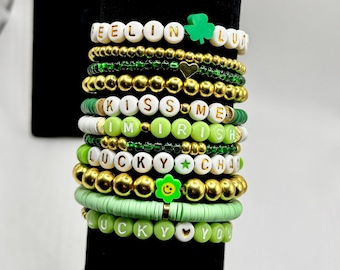 May include: A stack of beaded bracelets in shades of green and gold. Some bracelets have white letter beads spelling out phrases like "FEELIN LUCKY", "KISS ME I'M IRISH", and "LUCKY YOU". Charms include a shamrock and a smiley face.