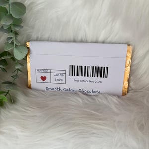 May include: A wrapped chocolate bar with a white label featuring a barcode and the text "Best Before Nov 2026." The label also includes a heart symbol and the words "100% Love." The words "Smooth Galaxy Chocolate" are printed at the bottom.