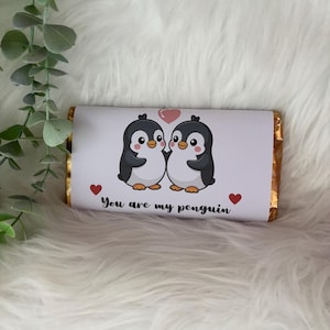 May include: A chocolate bar wrapped in white paper featuring two cartoon penguins with a pink heart above them. The text "You are my penguin" is printed below the penguins, with red heart accents.