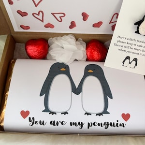 May include: A gift box with a chocolate bar featuring two penguin illustrations holding hands, with the text "You are my penguin." The box also contains heart-shaped chocolates, a white flower, and a card with a penguin pin.