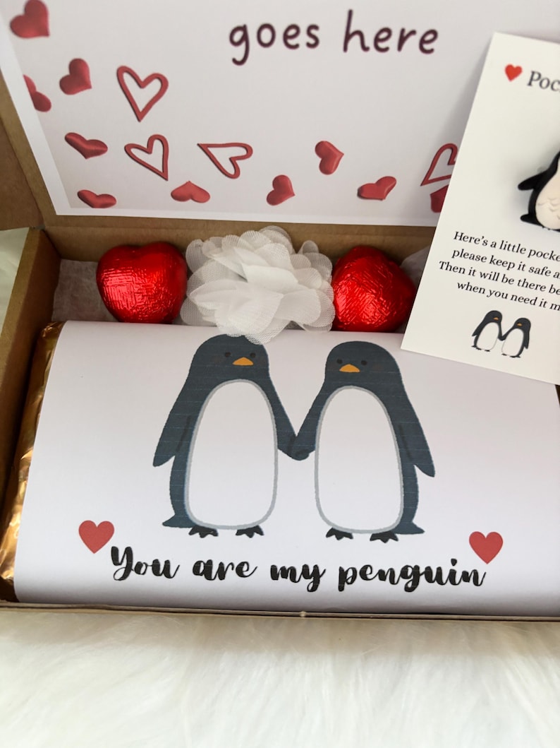 May include: A gift box with a chocolate bar featuring two penguin illustrations holding hands, with the text "You are my penguin." The box also contains heart-shaped chocolates, a white flower, and a card with a penguin pin.