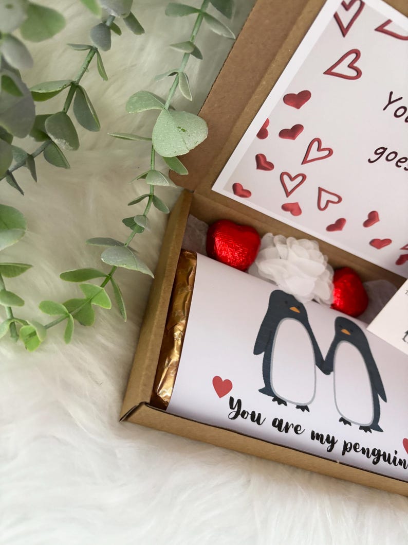 May include: A gift box with a white card featuring two penguin illustrations holding hands, with the text "You are my penguin". The box contains a chocolate bar, red foil-wrapped heart-shaped candies, and a white flower.