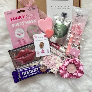 May include: A gift box containing a pink Funky Foil sheet mask, a Japan Sakura hair mask, a green Canyah pouch, a lip gloss, a Cadbury instant hot chocolate packet, a pink scrunchie with a candle, heart sponges, and a Christmas card.