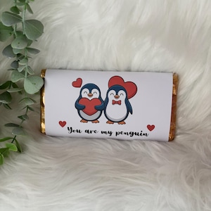 May include: A chocolate bar wrapped in gold foil with a white paper label. The label features two cartoon penguins holding red hearts, with the text "You are my penguin" and small red hearts.