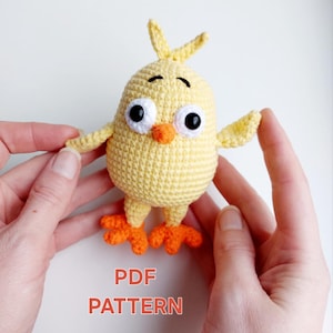 Puede incluir: Un juguete de pollito amarillo tejido a crochet con patas naranjas y grandes ojos negros. El juguete está siendo sostenido por dos manos. El texto "PDF PATTERN" está escrito debajo del juguete.
