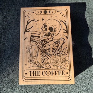 May include: A wooden box with a black and white illustration of a skeleton drinking coffee. The box has a moon and star design and the text "THE COFFEE" on the front.