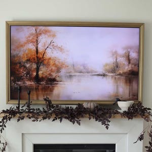 May include: A living room scene featuring a white fireplace with a framed landscape painting above. The mantel is decorated with dark burgundy foliage, a small pumpkin, and a white bowl. A wooden coffee table holds decorative items, including a white vase.