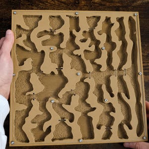 May include: A tan and clear acrylic ant farm with a maze-like interior. The ant farm has a rectangular shape with a series of interconnected chambers and tunnels. The design includes small metal screws and a textured surface.