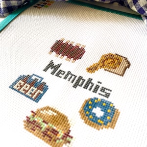 May include: Cross-stitch embroidery with the word "Memphis" and images of barbecue ribs, a donut, a burger, and a beer bottle.