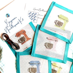 May include: A beginner needlepoint kit featuring printed instructions and five square canvas pieces with teal fabric borders. Each canvas displays a cross-stitched stand mixer in various colors including orange, lime green, pink, blue, and yellow.