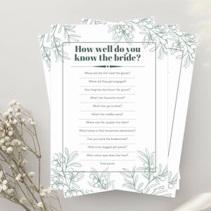 May include: Printable bridal shower game with a green floral border. The game asks questions about the bride, such as where she first met the groom, where they got engaged, and what her favourite movie is. The game includes a section for total points.