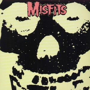 May include: A black and yellow graphic featuring a skull with the word "MISFITS" in pink above it. The skull has large eye sockets and a prominent nose. The background is a pale yellow color.