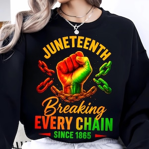 May include: Black sweatshirt with a Juneteenth graphic. The design shows a clenched fist in red, yellow, and green, breaking chains. Text includes "Juneteenth" and "Breaking Every Chain Since 1865."