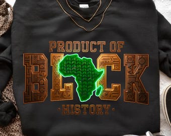 Puede incluir: Sudadera negra con el texto "PRODUCT OF BLACK HISTORY" en un diseño dorado y verde. La palabra "BLACK" presenta un mapa de África verde. Un collar dorado está drapeado sobre la sudadera.