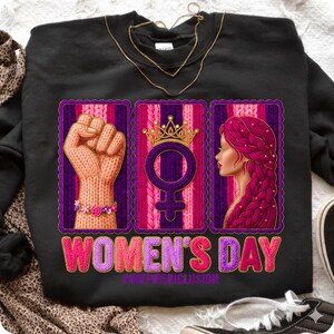 May include: Black sweatshirt with a graphic celebrating Women's Day. The design includes a knitted fist, a female symbol with a crown, and a woman's profile with braided hair. The text "WOMEN'S DAY" is in pink.