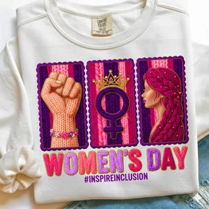 May include: White sweatshirt with a graphic celebrating Women's Day. The design includes a raised fist, a female symbol with a crown, and a woman's profile, all framed in purple. The text "WOMEN'S DAY" and "#INSPIREINCLUSION" are also featured.