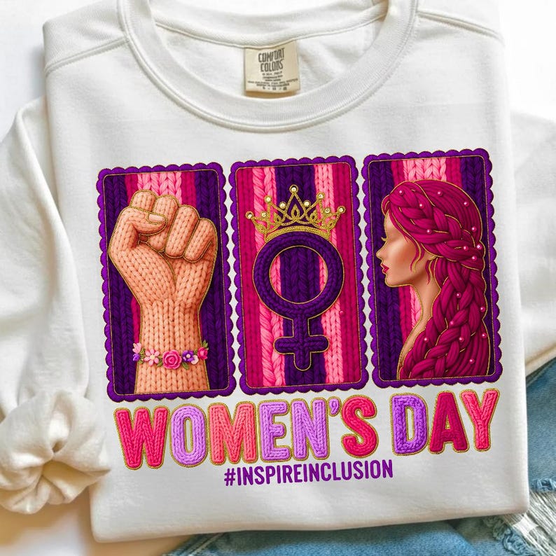 May include: White sweatshirt with a graphic celebrating Women's Day. The design includes a raised fist, a female symbol with a crown, and a woman's profile, all framed in purple. The text "WOMEN'S DAY" and "#INSPIREINCLUSION" are also featured.