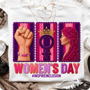 May include: White sweatshirt with a graphic design for Women's Day. The design includes a raised fist, a female symbol with a crown, and a woman's profile, all framed in purple. The text "WOMEN'S DAY" and "#INSPIREINCLUSION" are also featured.