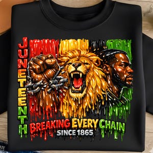 May include: Black sweatshirt with a vibrant graphic celebrating Juneteenth. The design features a clenched fist breaking chains, a roaring lion, and a portrait of a man, with text that reads "Juneteenth Breaking Every Chain Since 1865."