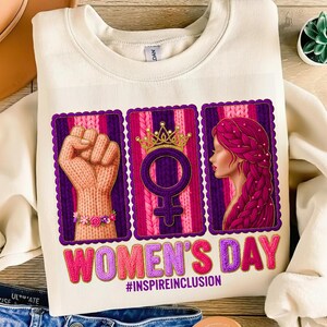 May include: Cream-colored sweatshirt with a graphic celebrating Women's Day. The graphic features a raised fist, a Venus symbol with a crown, and a woman's profile, all framed in purple. The text "WOMEN'S DAY" and "#INSPIREINCLUSION" are also displayed.