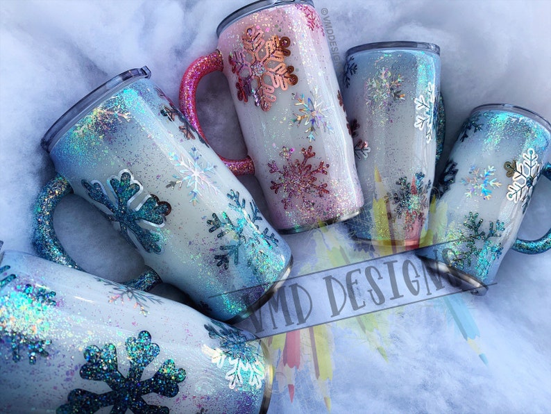 May include: Set of five stainless steel tumblers with a white base and snowflake designs. The tumblers have a glittery finish in shades of blue, pink, and white. The tumblers have a handle and are perfect for hot or cold beverages.