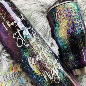 May include: Two stainless steel tumblers with a galaxy-inspired design. The larger tumbler has the text "Have Courage and Be Kind" on it. The smaller tumbler has the text "I have heard the stars too faintly to be fearful of the night".