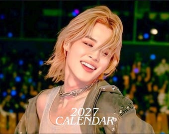 Könnte beinhalten: Ein Kalender für 2027 mit dem Porträt einer Person mit schulterlangem blondem Haar, die ein weißes Unterhemd, eine mehrlagige silberne Kettenhalskette und eine olivgrüne Jacke mit Metallnieten trägt und vor einem dunklen Hintergrund lächelt.