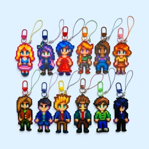 Op de afbeelding: Een collectie van twaalf pixel art karakter sleutelhangers, elk met een uniek figuur met verschillende haarkleuren, kledingstijlen en accessoires. Elke sleutelhanger bevat een kleurrijke plastic sluiting en een dun koordje.
