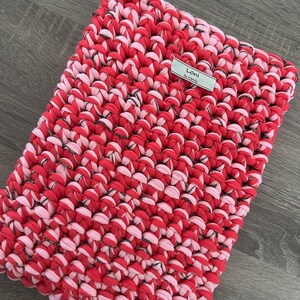 Peut inclure: Un tapis crocheté rose et rouge avec un fil argenté tissé dans toute sa longueur. Le tapis porte une étiquette indiquant "Lori by Mandy".