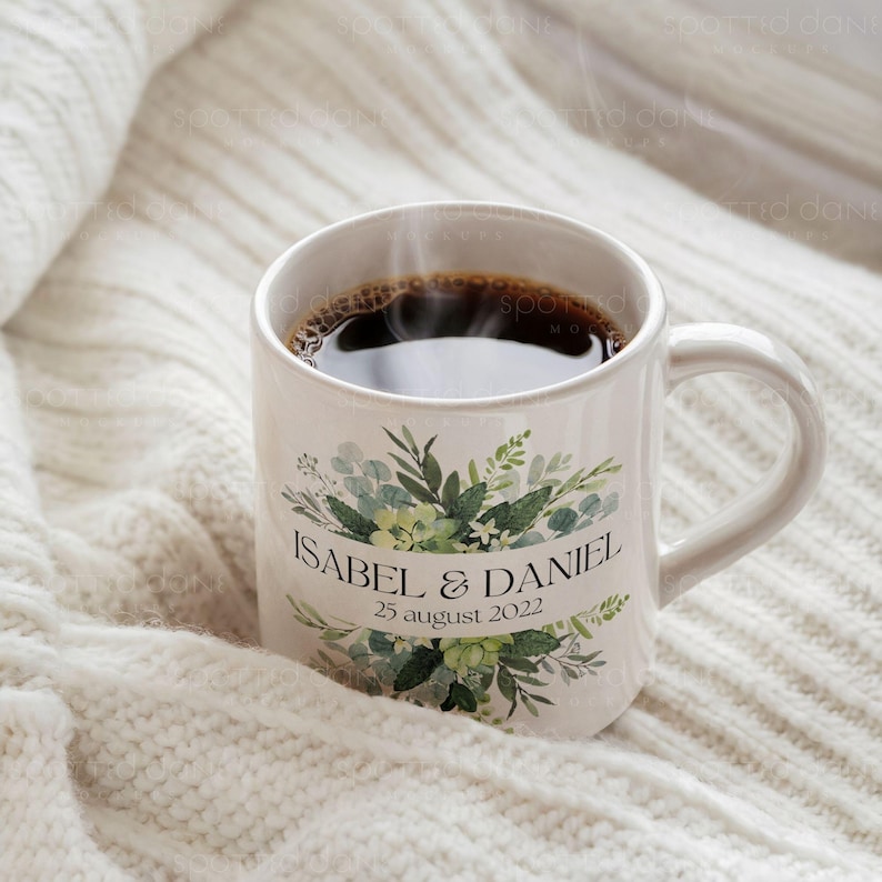 K&ouml;nnte beinhalten: Wei&szlig;e Keramiktasse mit gr&uuml;nem Blumendesign und dem Text "Isabel & Daniel 25. August 2022". Die Tasse ist mit Kaffee gef&uuml;llt und Dampf steigt aus der Oberseite auf.