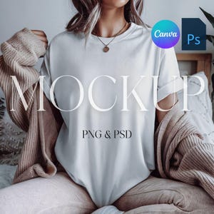 Könnte beinhalten: Ein weißes T-Shirt-Mockup mit einem einfachen Design, getragen von einer Person, die auf einem Bett sitzt. Der Text "MOCKUP" und "PNG & PSD" ist auf dem Shirt sichtbar.