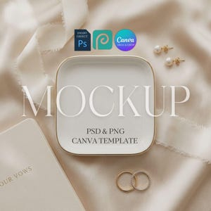 May include: A square white ceramic trinket dish with a gold rim, featuring the text MOCKUP, PSD & PNG CANVA TEMPLATE. The dish is accompanied by two gold rings and two pearl earrings, all set against a soft, draped cream-colored fabric.