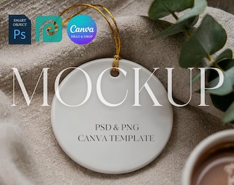 May include: A white, round ceramic ornament with a gold string for hanging. The word "MOCKUP" is printed on the front in a serif font. Below, the text reads "PSD & PNG CANVA TEMPLATE". The ornament is on a neutral-toned fabric.
