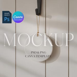 May include: A white, round ceramic ornament mockup hanging from a black hook with a gold string. The text "MOCKUP" is displayed in large, light gray letters. Below, the text reads "PSD & PNG CANVA TEMPLATE".